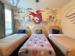 Een hotelkamer met twee bedden, een Spiderman muurschildering en een stadsgezicht wandontwerp.