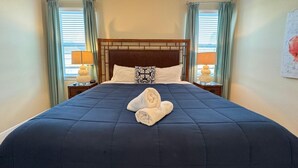 A neatly made bed with a dark blue bedspread and two pillows, flanked by two bedside tables with lamps, in a room with light-colored walls and curtains. - 7613-8-bl-only 10 Minutes From Disney (Kissimmee)