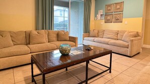 A living room with two beige sofas, a glass coffee table, and a view through a sliding glass door. - 7613-8-bl-only 10 Minutes From Disney (Kissimmee)