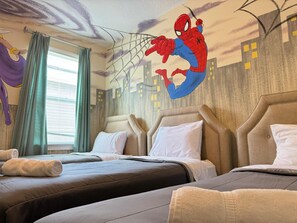 Een hotelkamer met twee bedden, een muurschildering van Spider-Man en een raam met gordijnen.