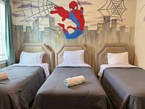 Een hotelkamer met drie bedden, elk voorzien van een hoofdeinde en witte kussens. Achter de bedden is een muurschildering van Spiderman te zien.