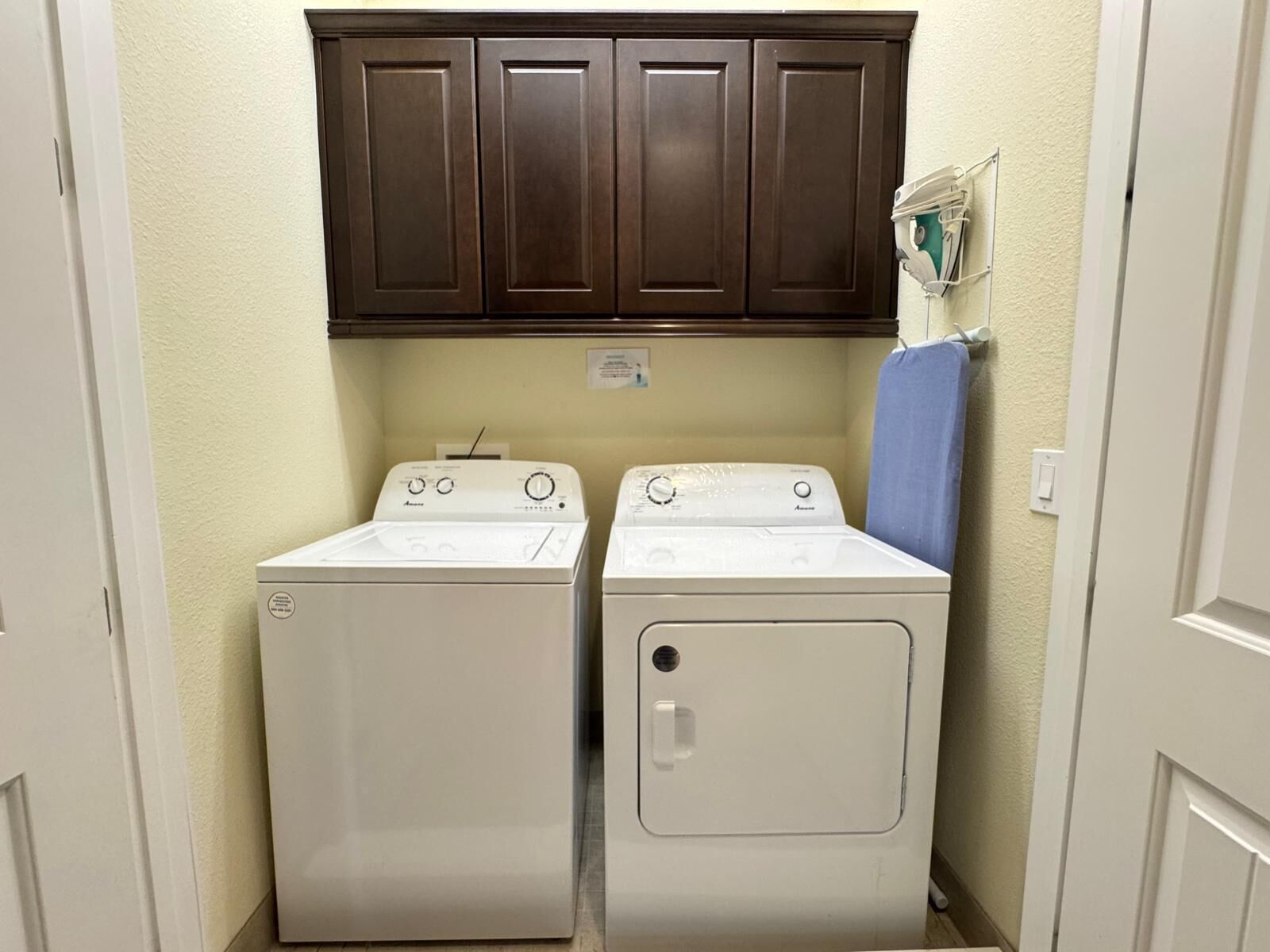 A laundry room with two white front-loading washers and a dark brown cabinet above them.