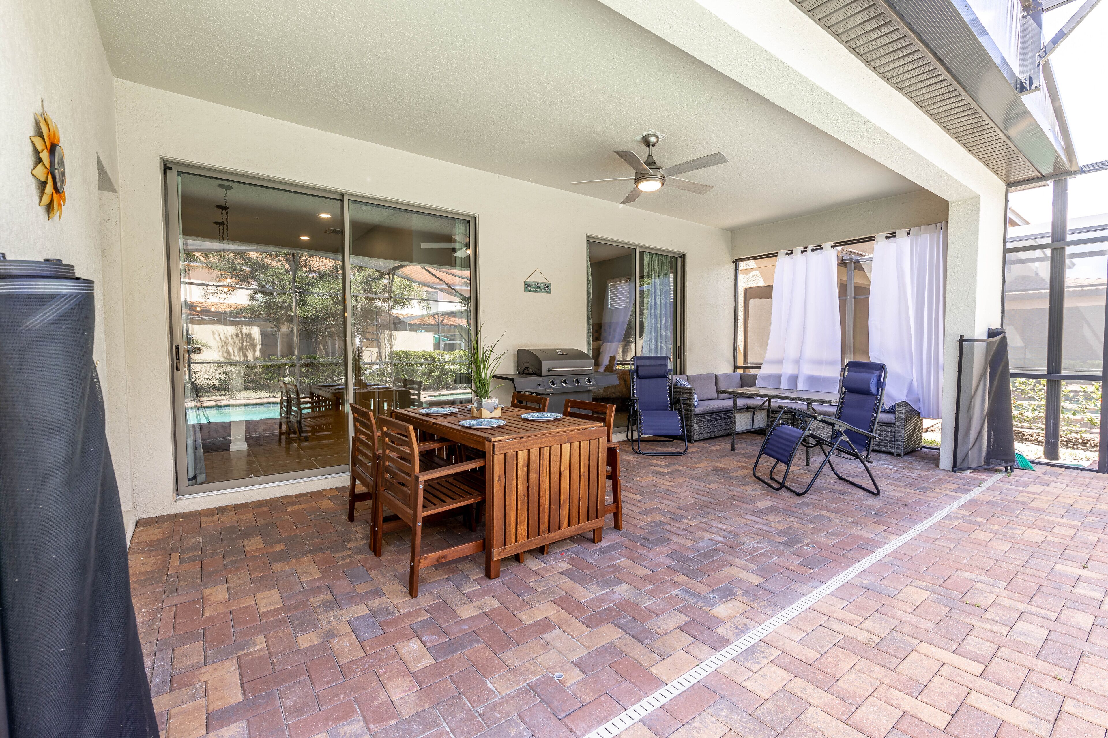 An outdoor patio with a wooden table and chairs, a ceiling fan, and a grill.