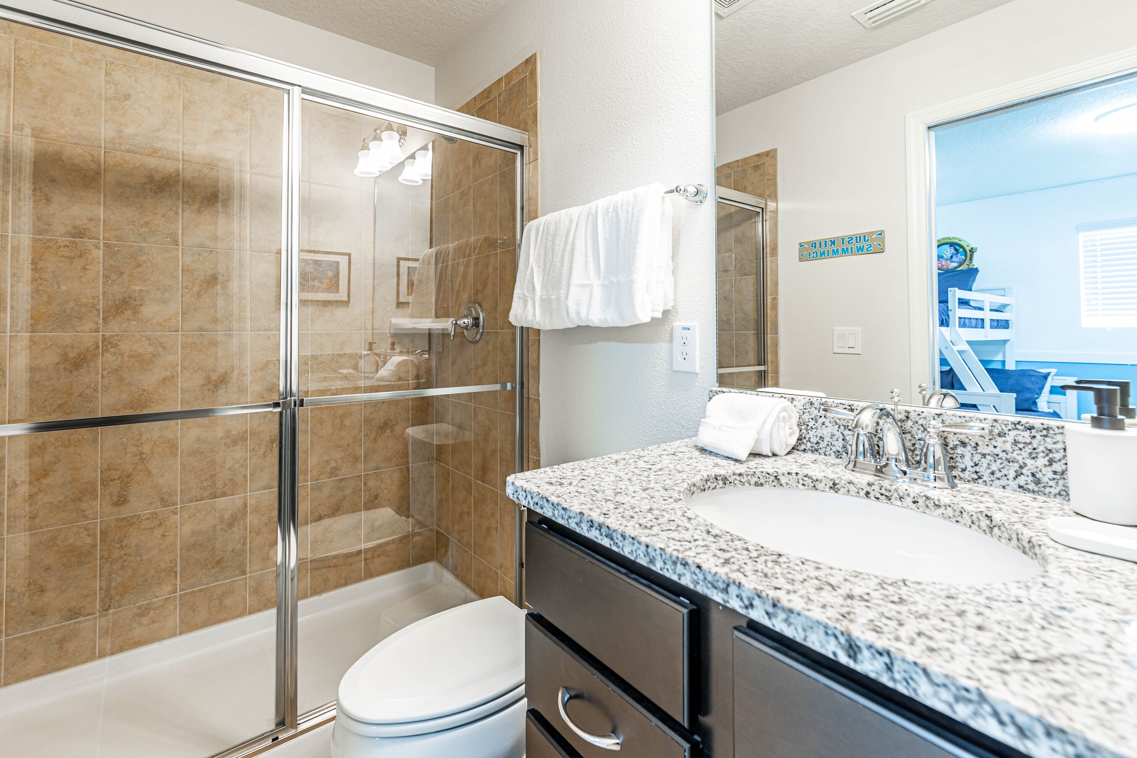 Ein modernes Badezimmer mit einer Duschkabine aus Glas, einer weißen Toilette, einem Waschbecken mit Granitplatte und einem großen Spiegel.
