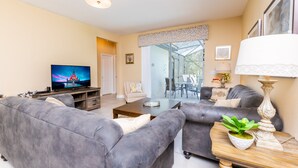 Ein Wohnzimmer mit einer Couch, einem Fernseher, einem Couchtisch und einem Essbereich mit Stühlen und einem Tisch.