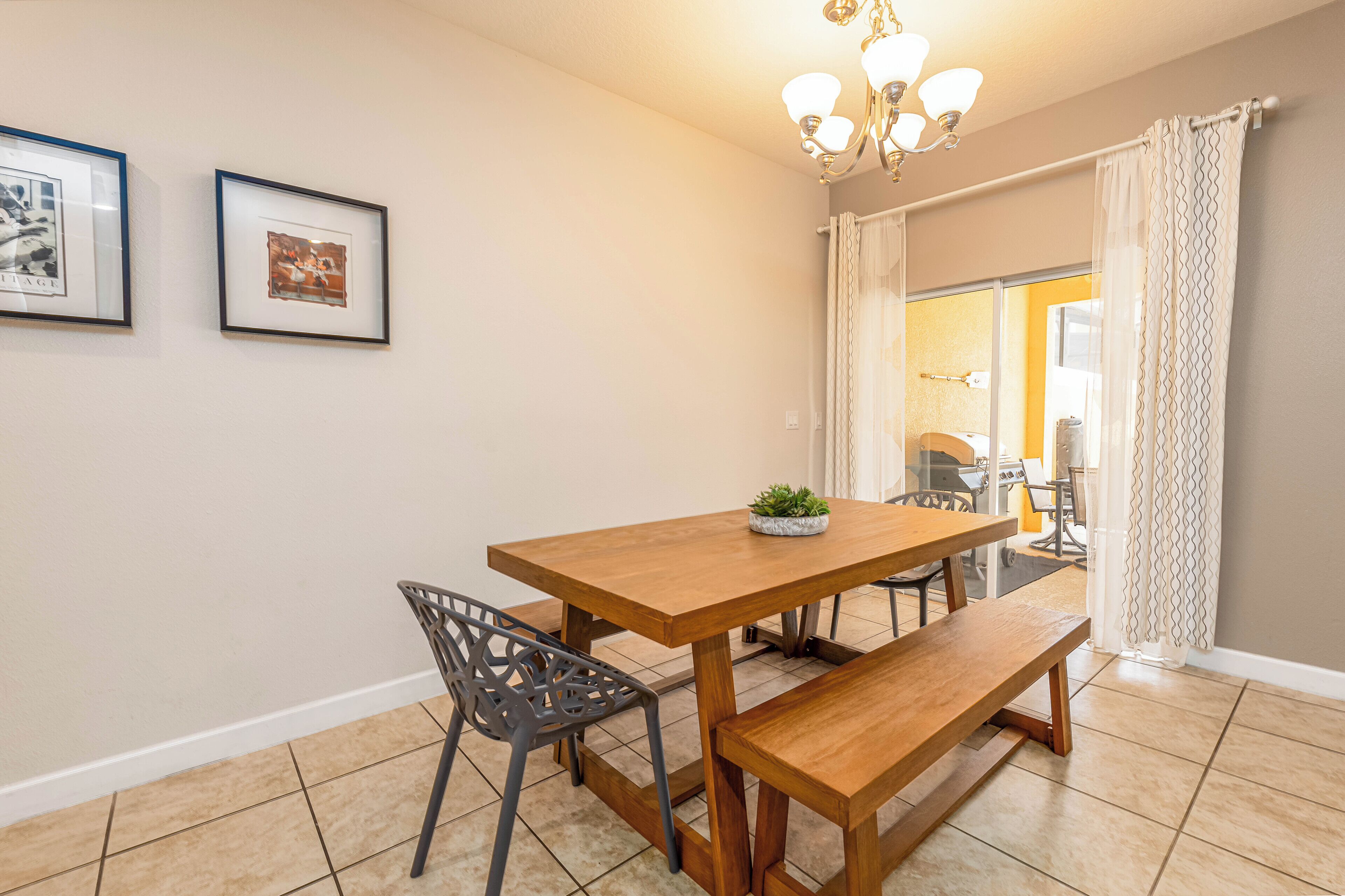 Un comedor con una mesa de madera, dos sillas, un banco, una lámpara de araña y dos cuadros en la pared.
