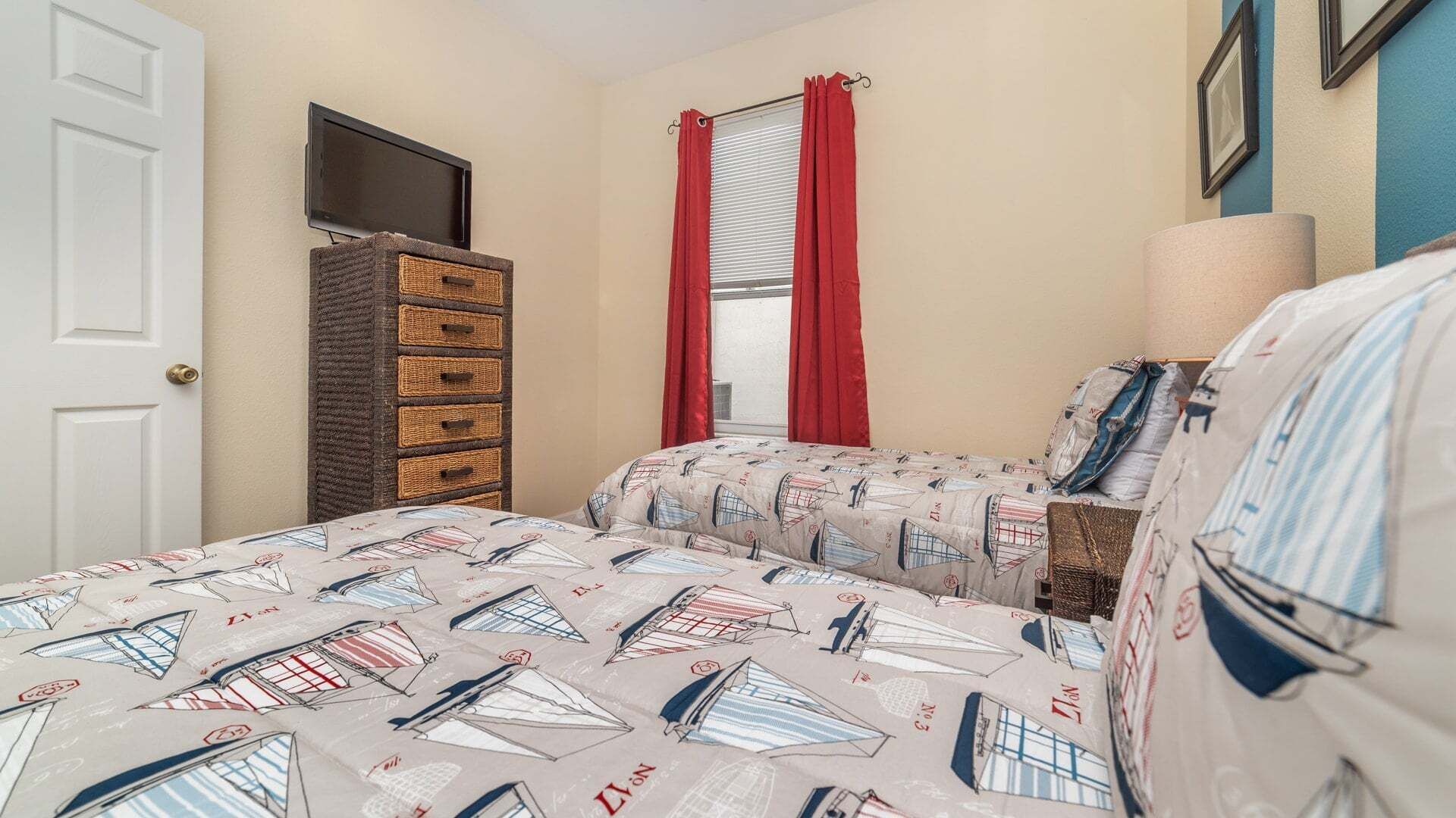 A bedroom with a bed, dresser, TV, window with curtains, and a lamp.