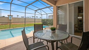 A covered patio with a glass table and chairs, a pool, and a view of the surrounding area. - Fp8190 Windsor Palms Resort Vacation Home (Kissimmee)