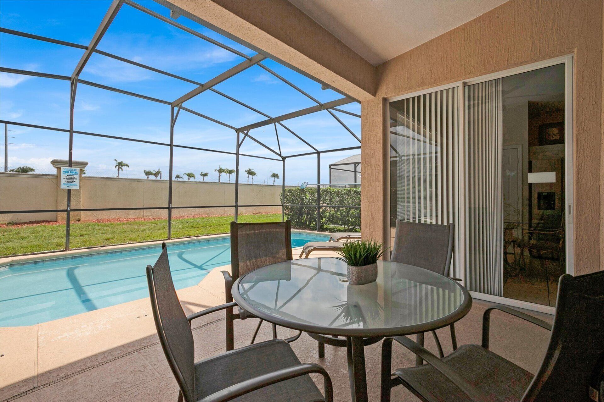 A covered outdoor area with a pool, a glass table, and chairs.