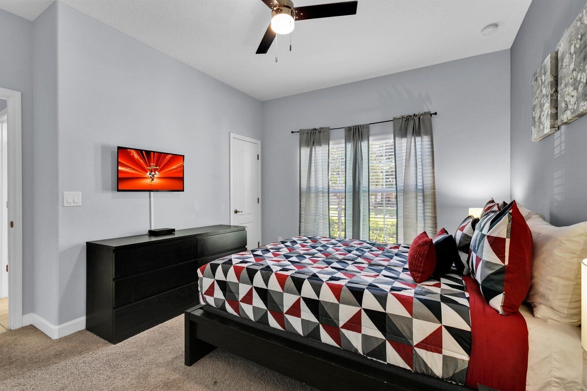 A bedroom with a bed, a TV, a ceiling fan, and a window with curtains.
