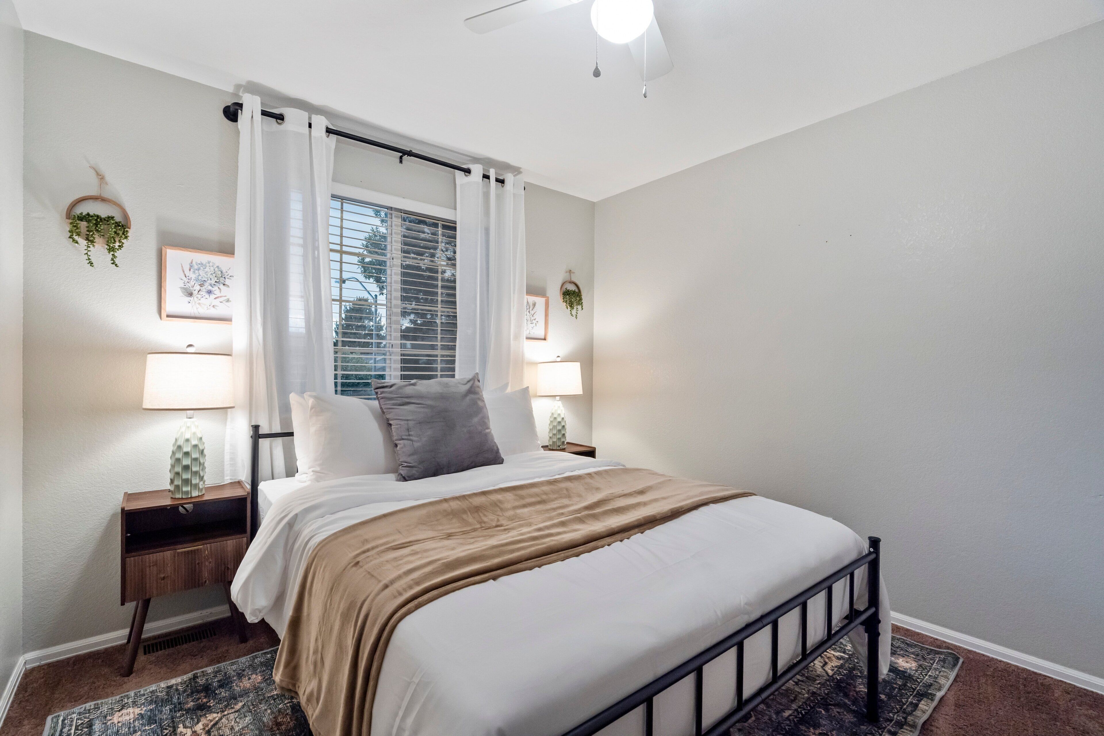 A neatly arranged bedroom with a bed, bedside lamps, and a window with curtains.