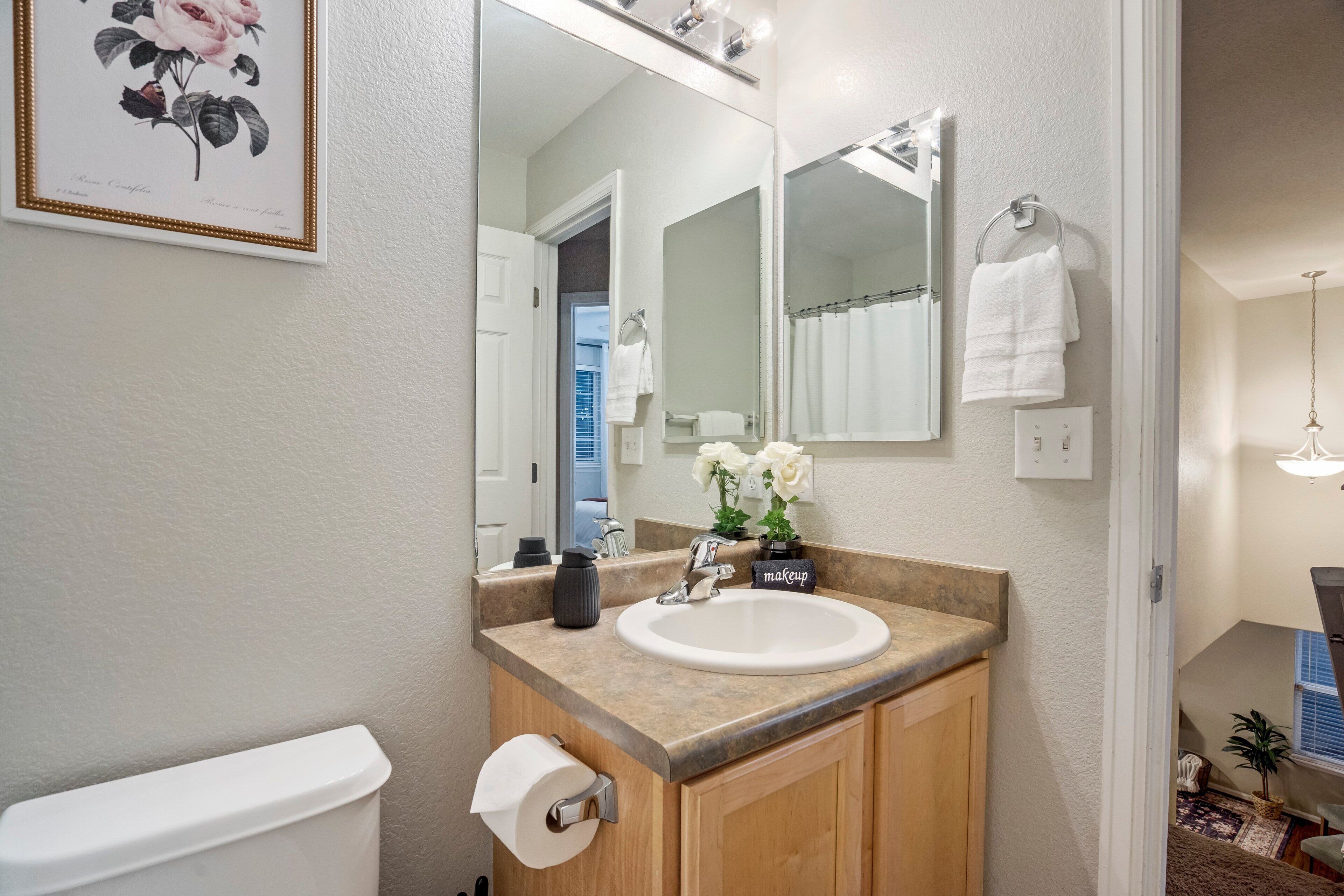 A bathroom with a sink, mirror, toilet, and a framed floral artwork.