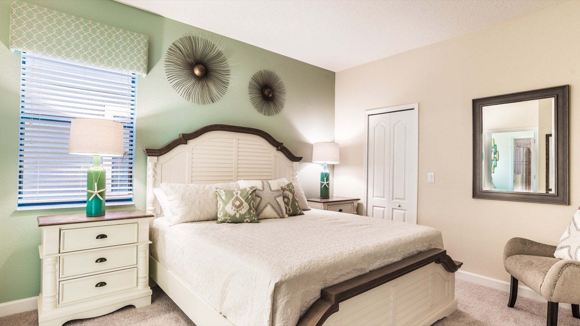A bedroom with a bed, bedside tables, a chair, a window with blinds, and a door.