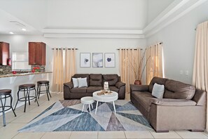 A modern living room with a brown leather sofa, a white coffee table, and a bar area with stools. - Rgc346 (Davenport)