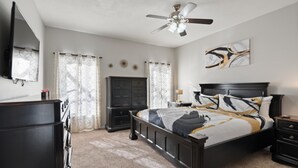 A bedroom with a bed, a dresser, a nightstand, a ceiling fan, and a TV mounted on the wall. - Rgc346 (Davenport)