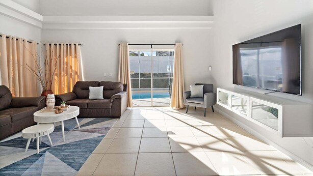 A spacious living room with a large TV, two sofas, a coffee table, and a view of a swimming pool. - Rgc346 (Davenport)
