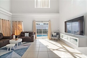 A spacious living room with a large TV, two sofas, a coffee table, and a view of a swimming pool. - Rgc346 (Davenport)