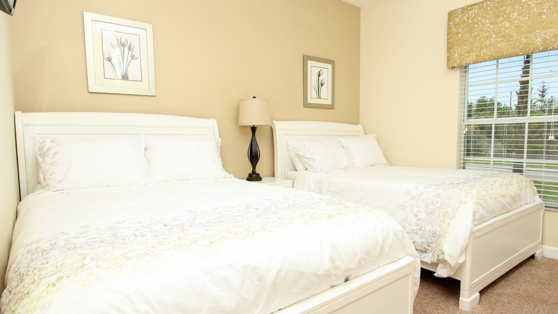 A room with two white beds, a nightstand with a lamp, and two framed floral pictures on the wall.
