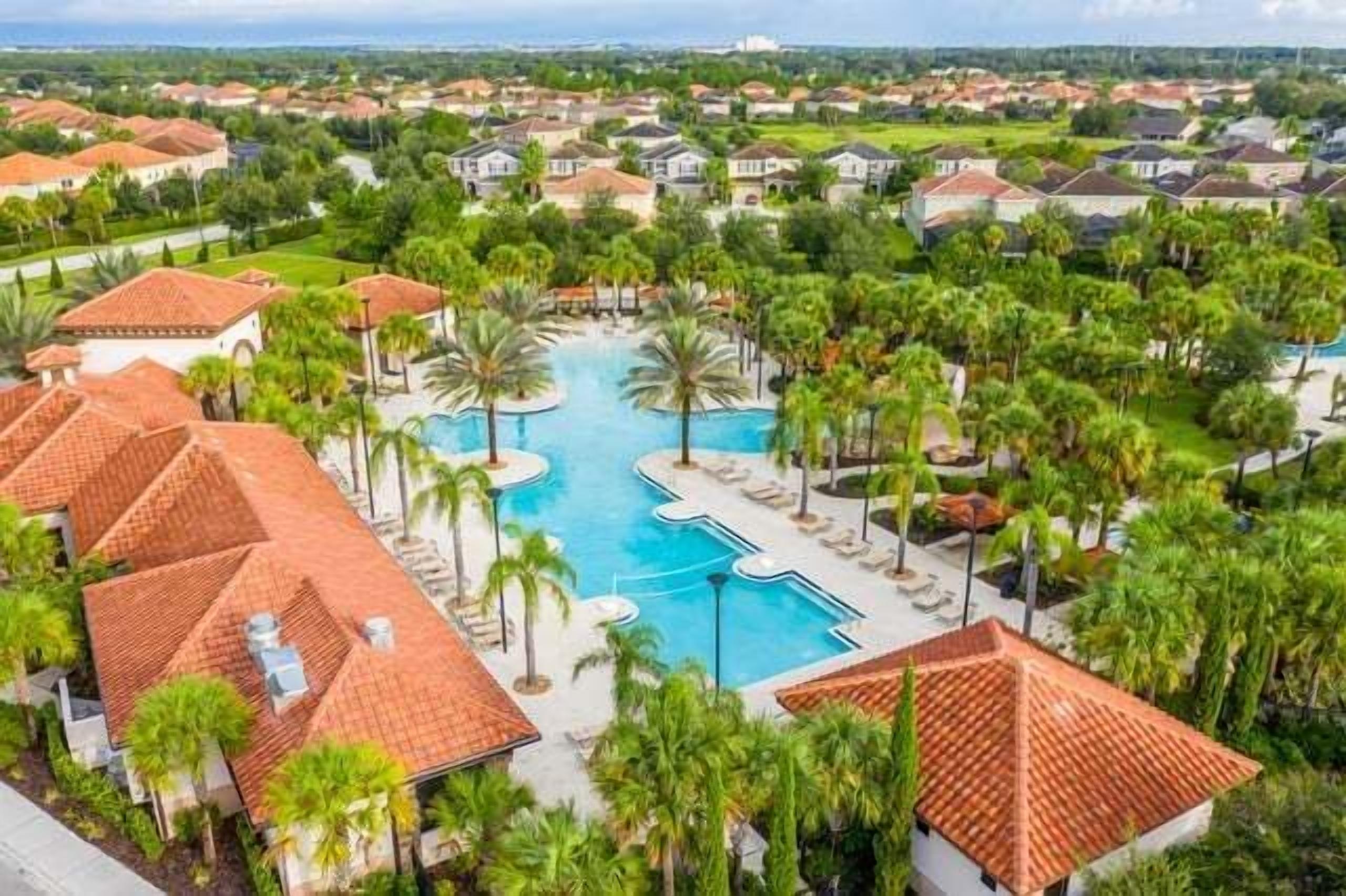 A resort with a central swimming pool, surrounded by palm trees and red-roofed villas.