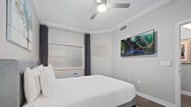 A bedroom with a bed, a ceiling fan, a window with curtains, and a painting on the wall. - Bk0203 Villas South Preserve (Kissimmee)
