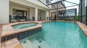 Een zwembad met een jacuzzi, buitenmeubilair en een overdekt gebied met glazen wanden.