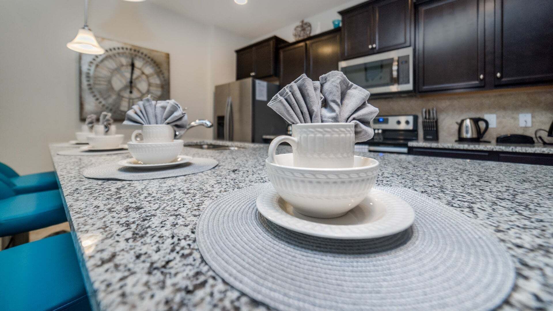 A kitchen with granite countertops, dark cabinets, and a clock on the wall.