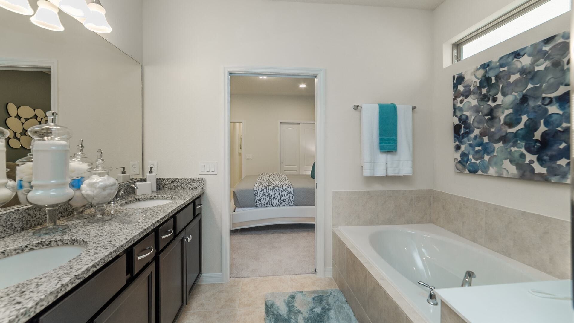 Une salle de bain moderne avec un meuble-lavabo à deux vasques, un grand miroir, une baignoire et un couloir menant à une chambre.