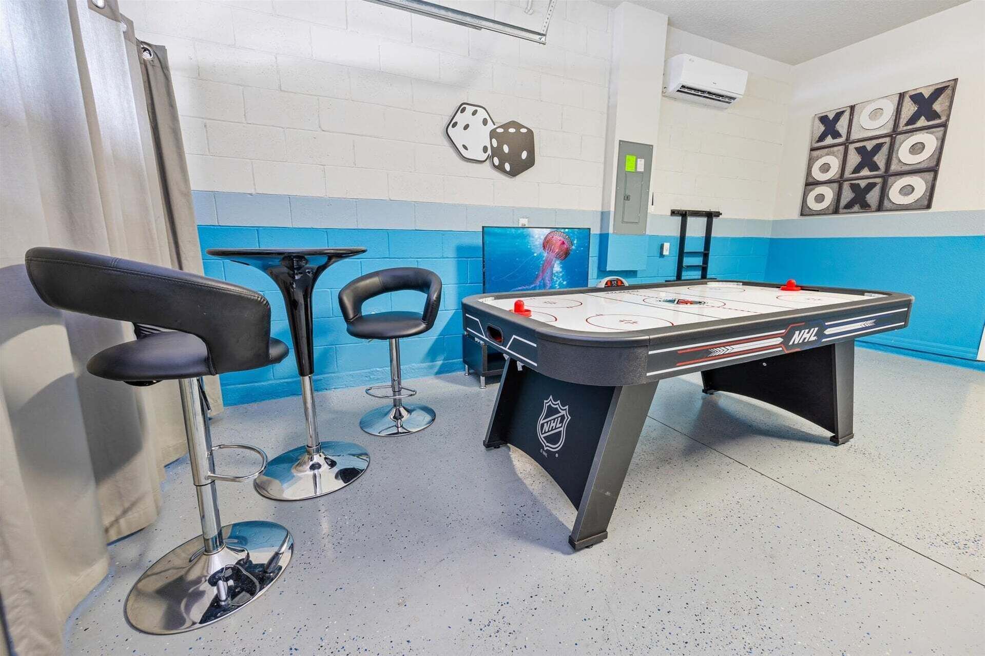 Een kamer met een tafelvoetbaltafel, twee barstoelen, een wandairconditioner en een blauw-wit kleurenschema.
