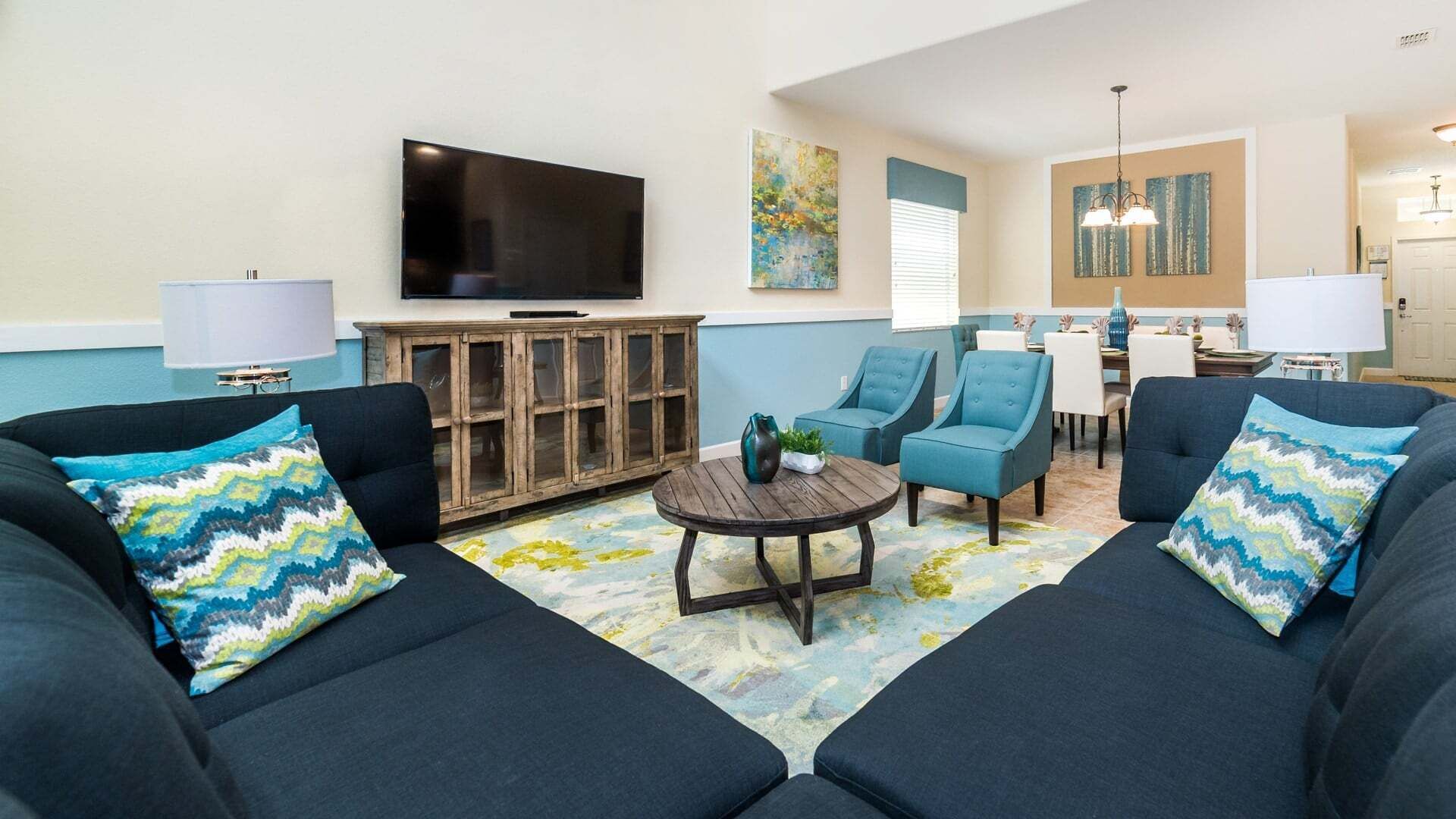 A living room with two sofas, a coffee table, and a TV. There is a dining area with chairs and a table.