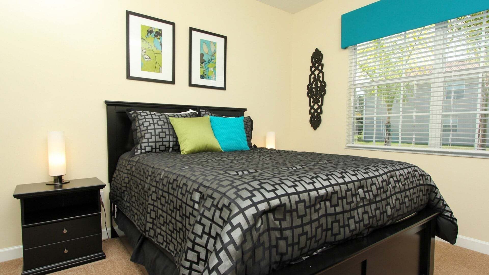 A bedroom with a bed, nightstands, a window with blinds, and two framed pictures on the wall.