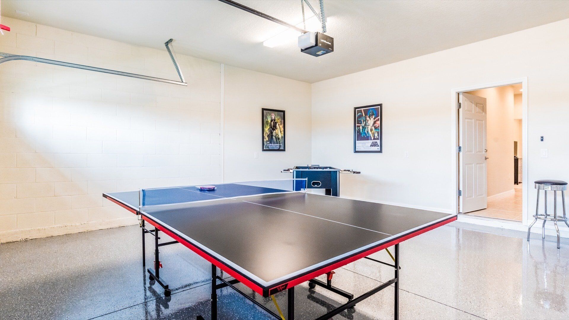 A ping pong table in a room with white walls, a projector, and two framed posters.