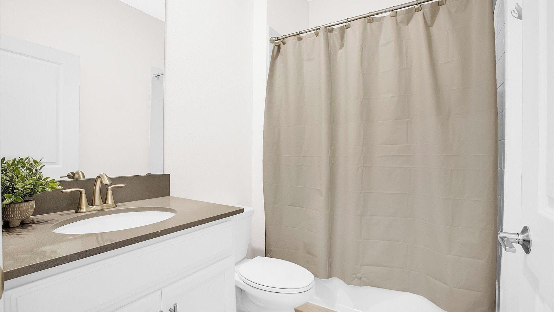 A bathroom with a white sink, a mirror, a toilet, and a beige shower curtain.