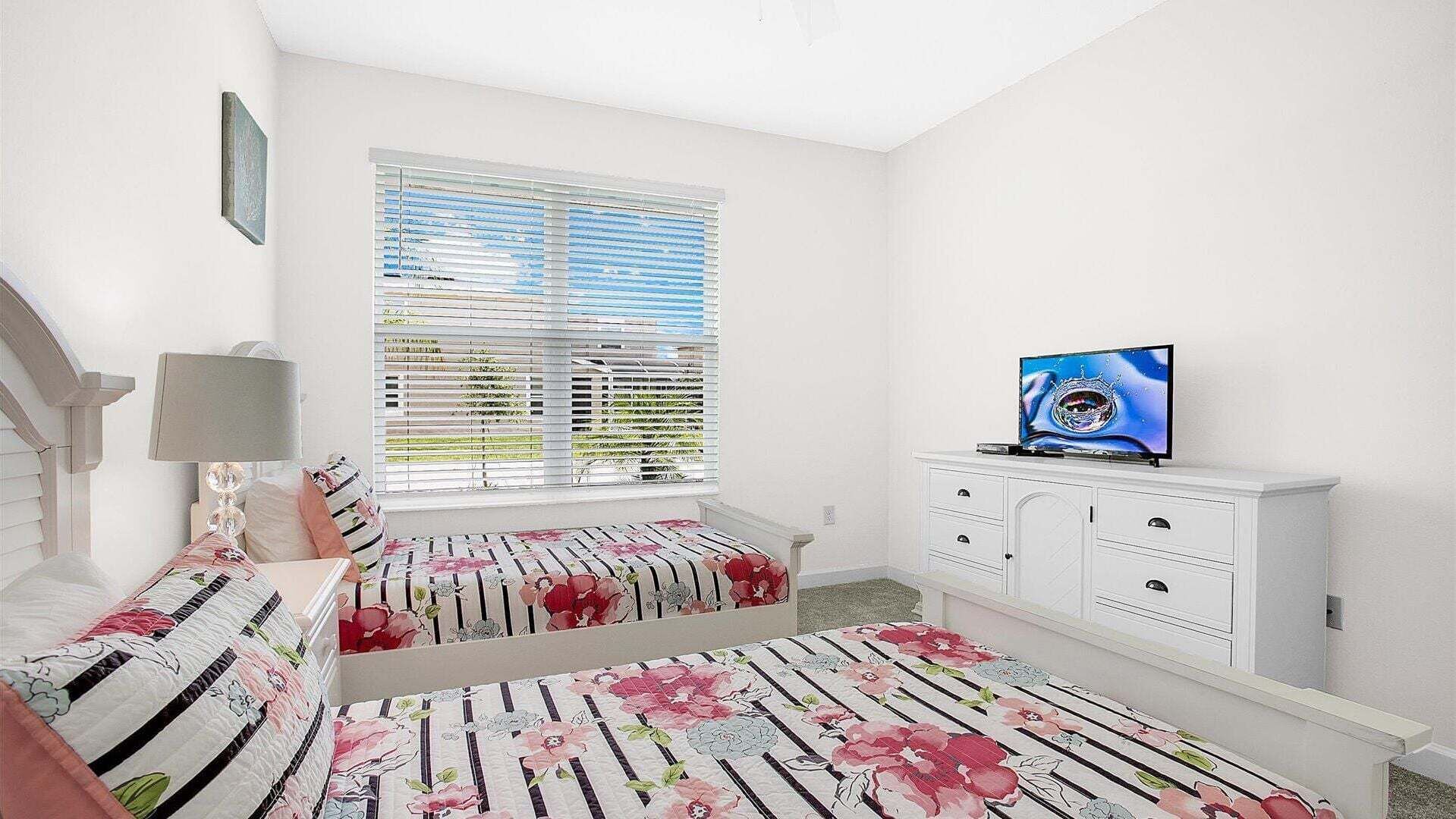 A bedroom with a bed, a TV on a dresser, a window with blinds, and a staircase.