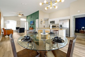 A modern kitchen with a central island, a dining area with a glass table, and a ceiling fan. - Pet-friendly Home w Pool Near Disney & Champions Gate (Davenport)