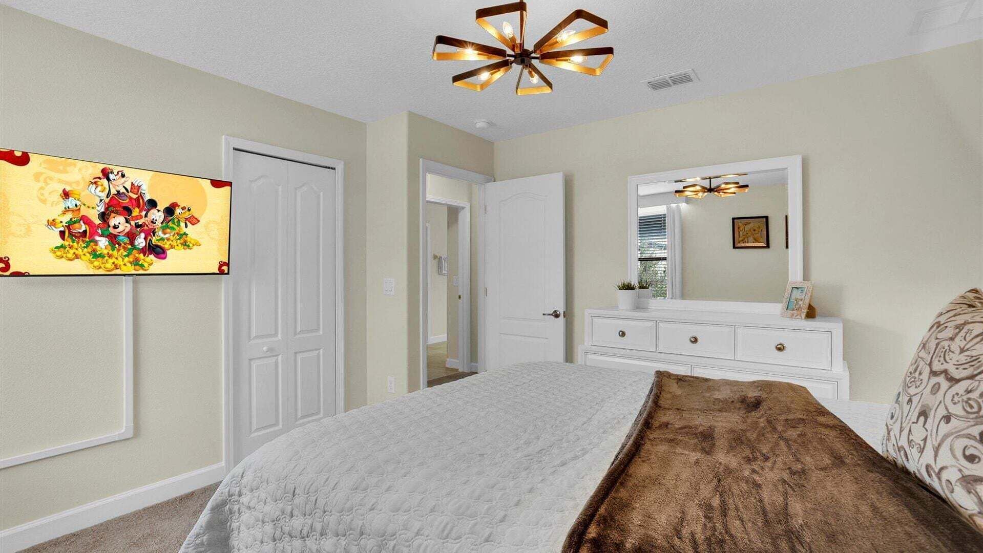 A bedroom with a bed, dresser, mirror, and a ceiling light fixture.