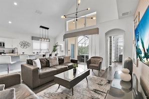Ein modernes Wohnzimmer mit einem Ecksofa, einem Glastisch und einem Essbereich, im Hintergrund befindet sich eine Küche.