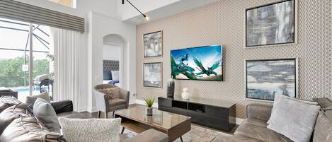 Una sala de estar moderna con un televisor de pantalla plana grande, sofás de cuero, una mesa de centro y una pared con estampado.