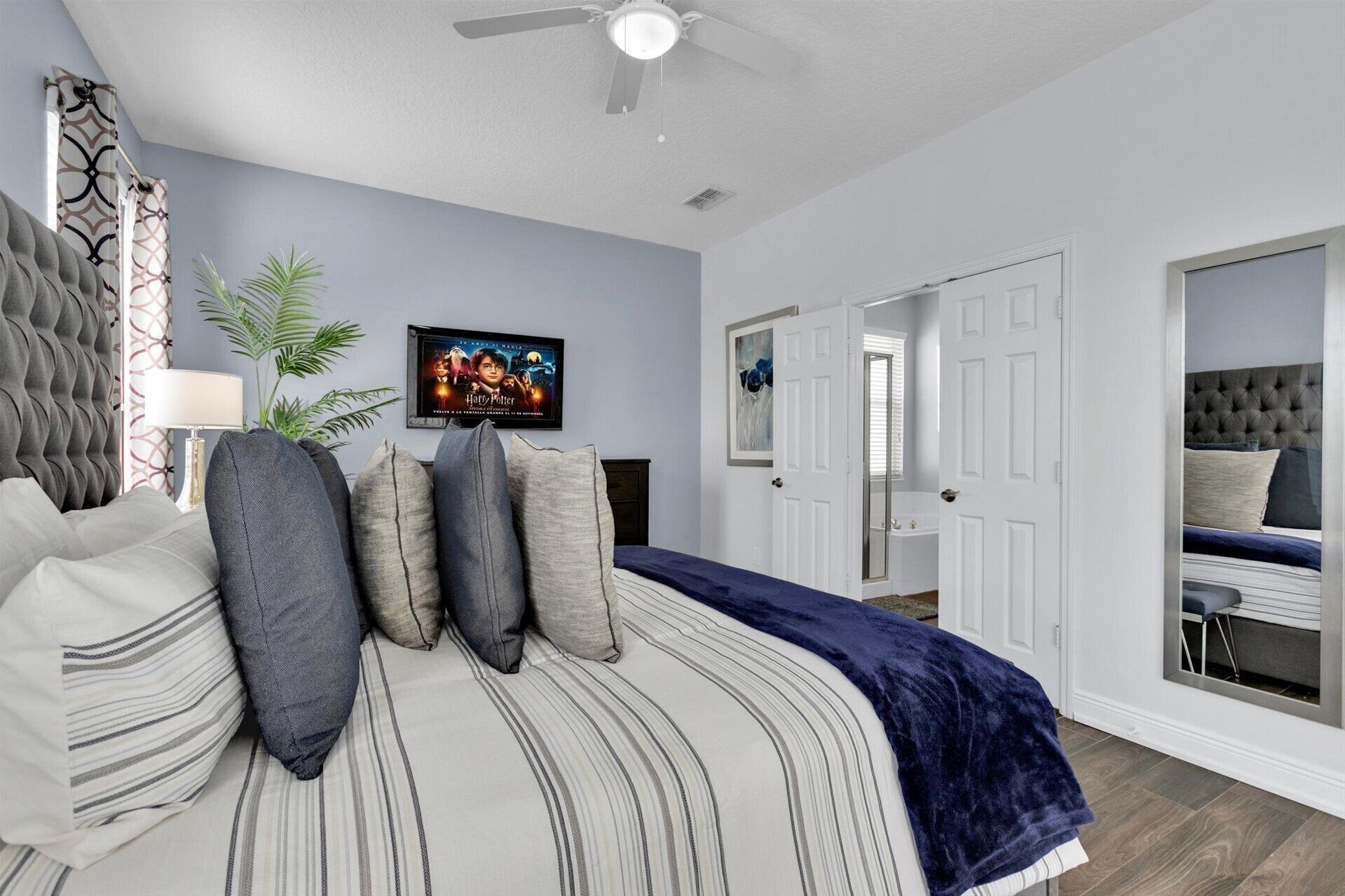 A bedroom with a bed, a ceiling fan, a wall-mounted picture, and a door leading to another room.