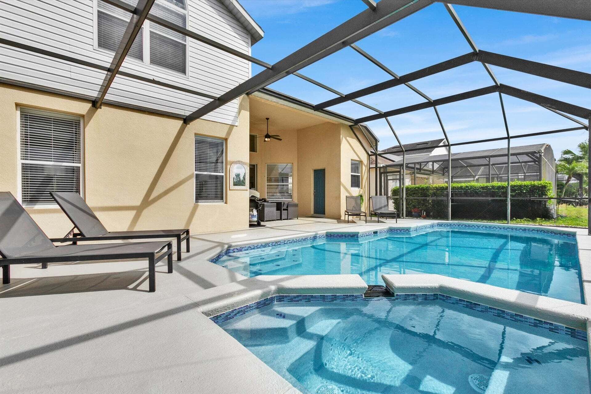 A swimming pool with a glass enclosure, lounge chairs, and a covered patio area.