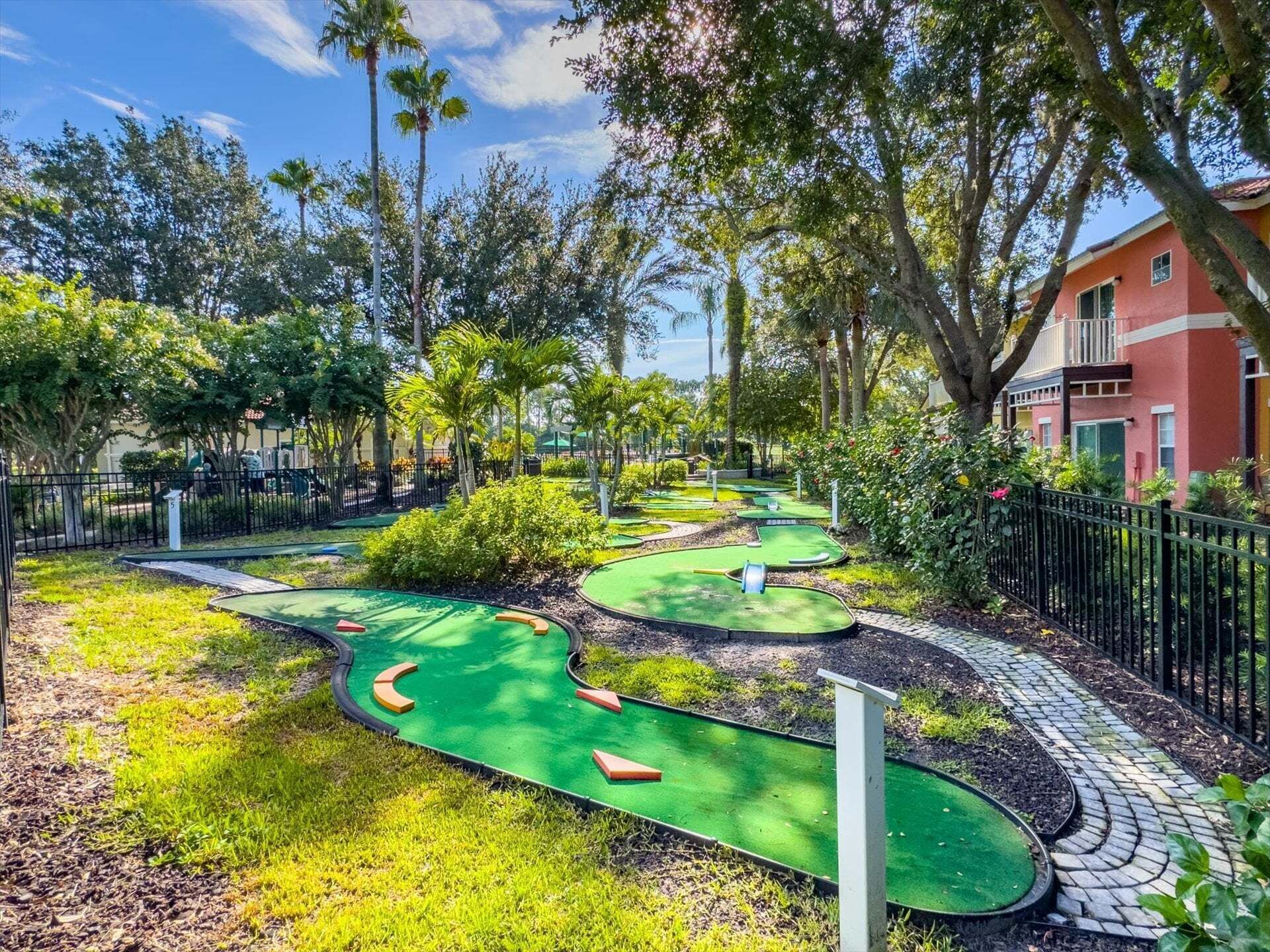 Un parcours de minigolf comportant plusieurs trous, entouré d’une végétation luxuriante et avec un bâtiment rouge en arrière-plan.