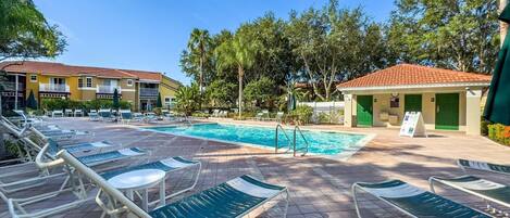 A pool area with lounge chairs, a swimming pool, and a building with a red-tiled roof.
