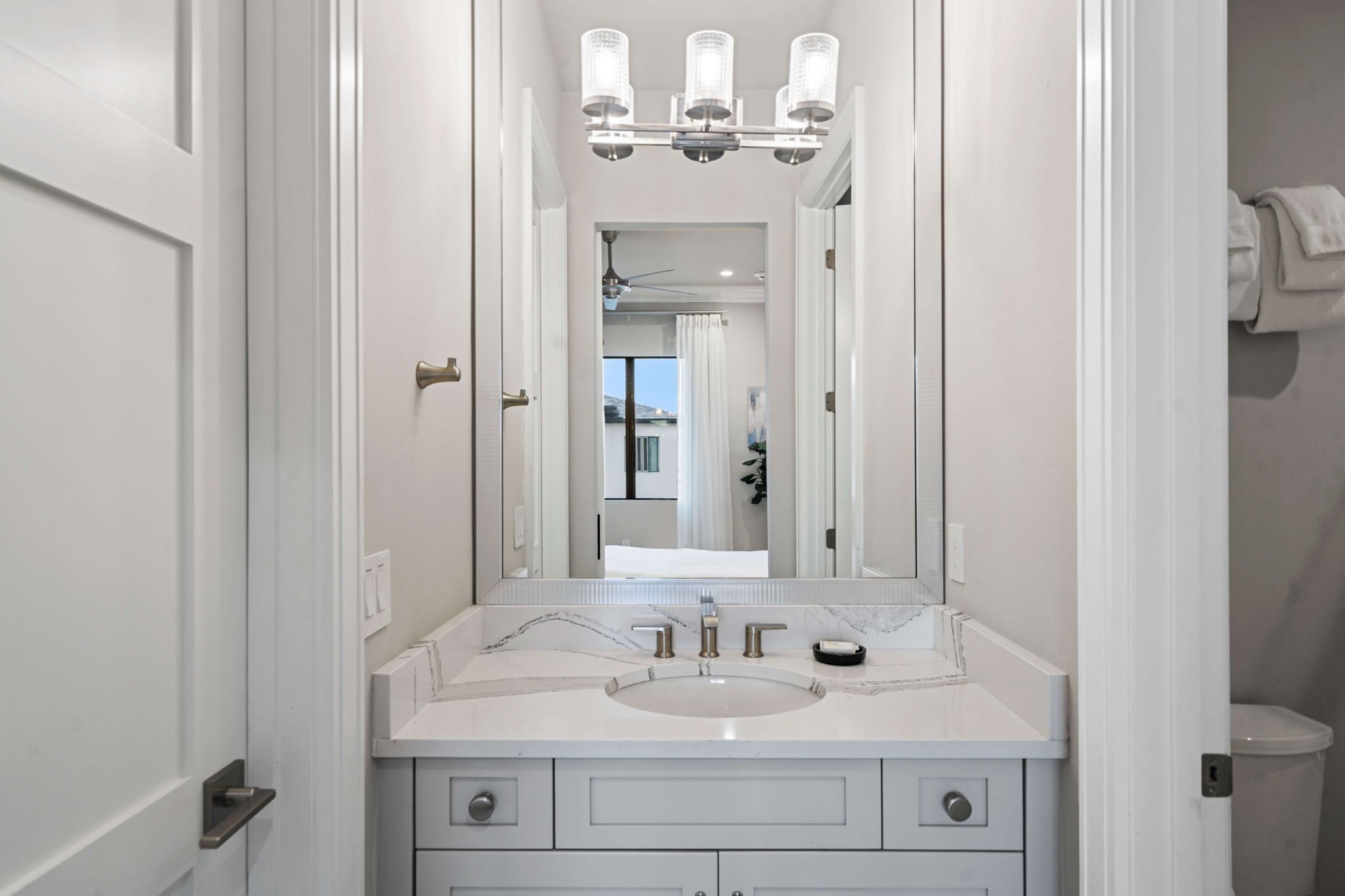 Une salle de bain moderne avec un meuble-lavabo blanc, un grand miroir et un luminaire fixé au plafond.