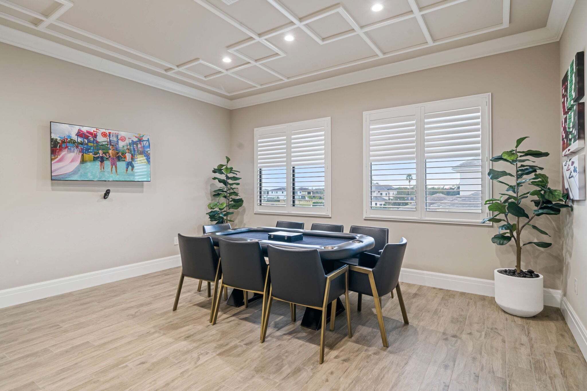 A conference room with a round table, chairs, a painting, windows, and potted plants.