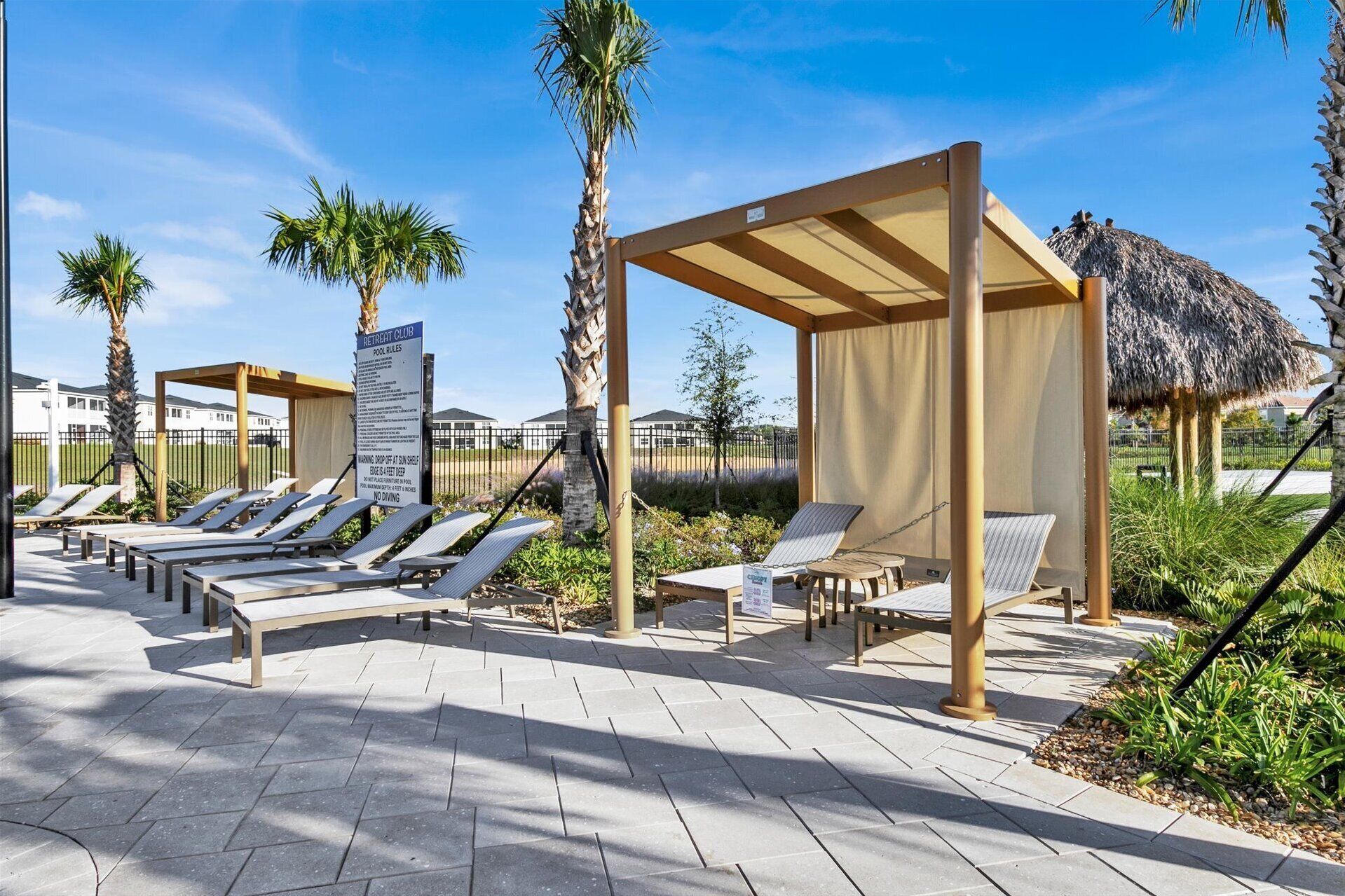 A poolside area with sun loungers, a covered seating area, and a sign indicating pool rules.