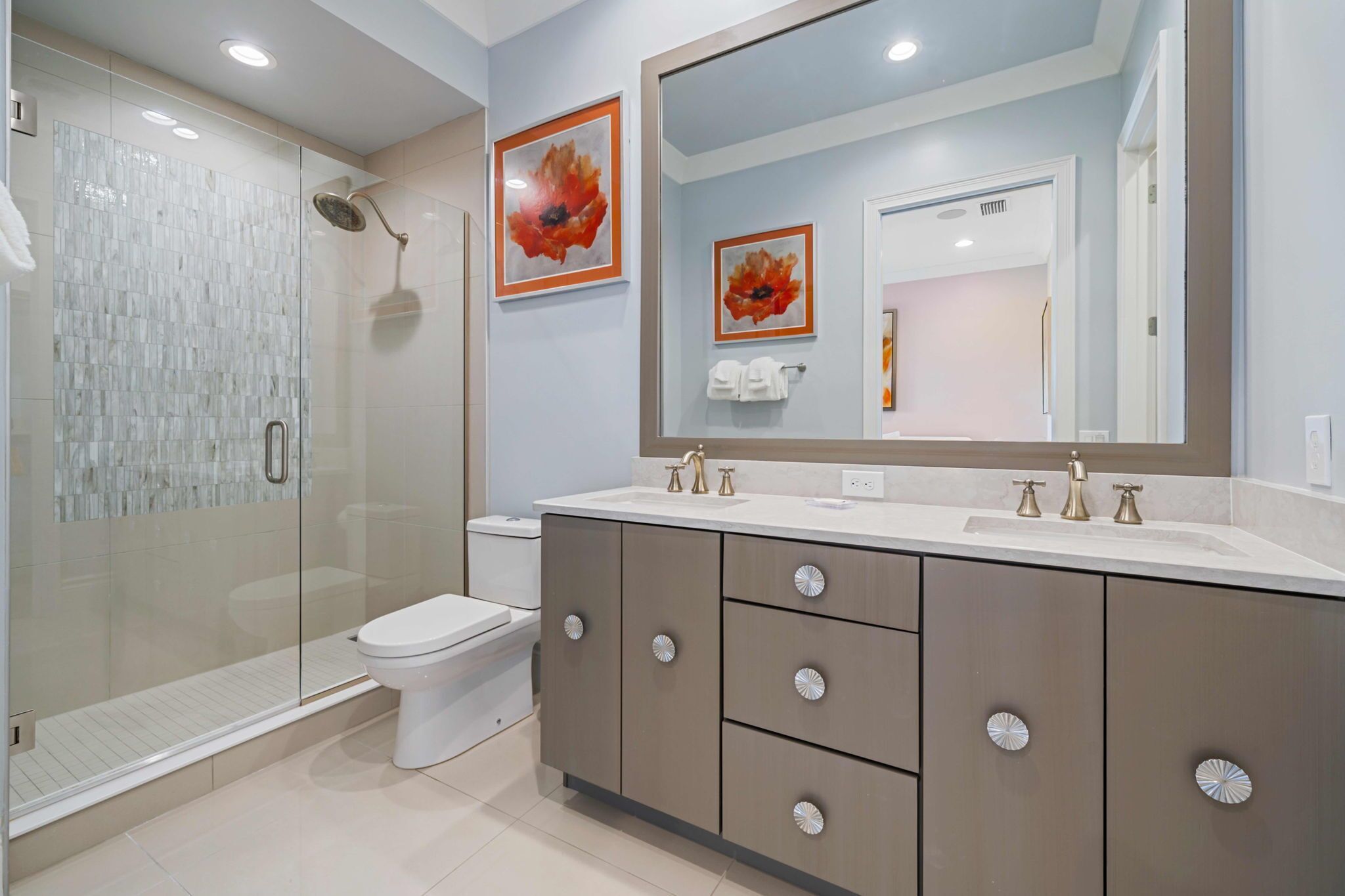 A modern bathroom with a glass-enclosed shower, a white toilet, and a vanity with a large mirror.