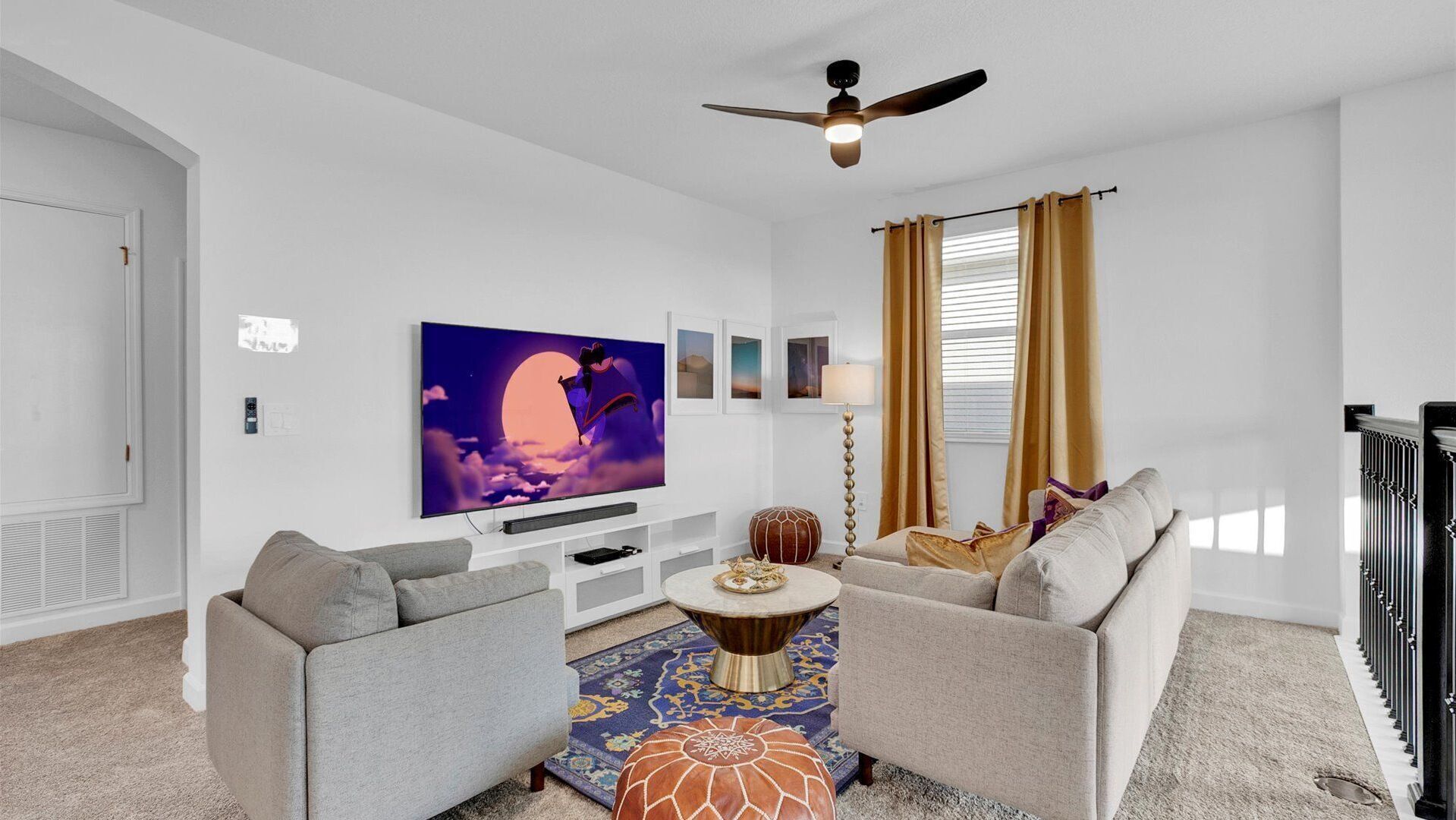 A modern living room with a flat-screen TV, grey sofas, a coffee table, and a patterned rug.