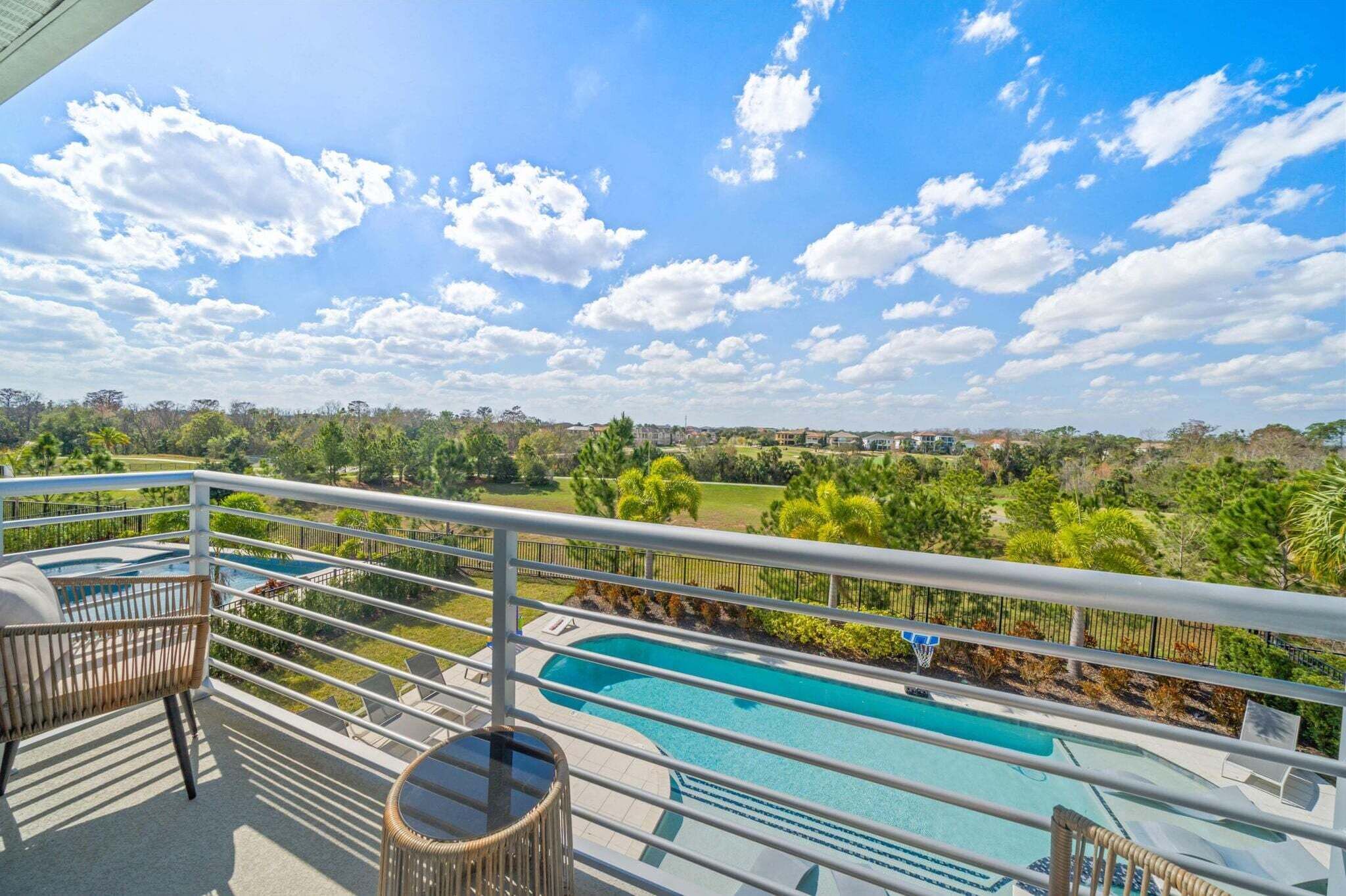 A balcony with a view of a swimming pool, a railing, and a chair.