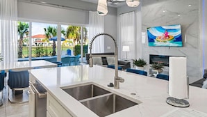 A modern kitchen with a large island, a built-in sink, and a flat-screen TV mounted on the wall. - Rc104p Fairway Bliss (Kissimmee)
