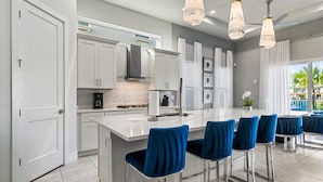 A modern kitchen with white cabinets, a central island, and blue bar stools. - Rc104p Fairway Bliss (Kissimmee)