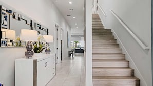 A modern hallway with a white console table, a staircase with wooden steps, and a view into a dining area. - Rc104p Fairway Bliss (Kissimmee)